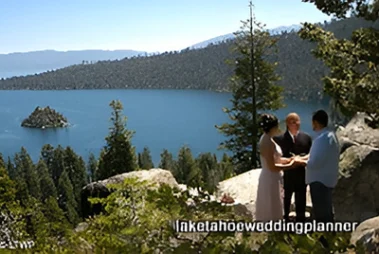 A couple getting married outdoors by a lake with an officiant, with a small island visible in the background.