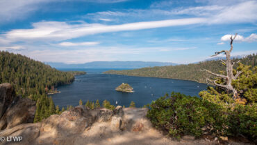 View of emerald bay at lake tahoe with fannette island in the center, surrounded by forested hills under a cloudy sky.