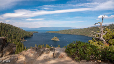 View of emerald bay at lake tahoe with fannette island in the center, surrounded by forested hills under a cloudy sky.