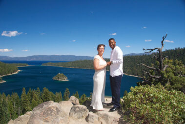 A couple standing on top of a mountain near the water.
