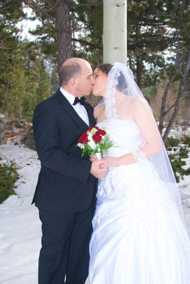 A bride and groom kissing in the snow.