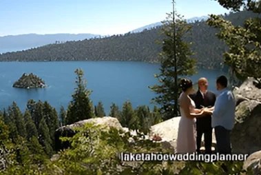 A couple exchanges vows by lake tahoe, with a small island visible in the lake and pine trees around, under the gaze of an officiant.