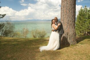 A bride and groom pose for a picture in front of the water.