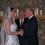 A bride and groom holding hands while the officiant looks on.