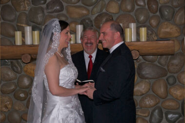 A bride and groom holding hands while the officiant looks on.