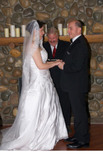 A bride and groom are holding hands while the officiant looks on.