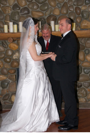 A bride and groom are holding hands while the officiant looks on.