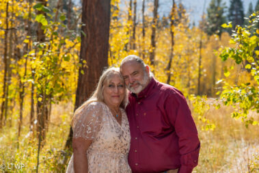 A couple embraces among autumn aspen trees, with golden leaves and sunlight in the background.