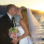 A bride and groom kissing on the side of a boat.